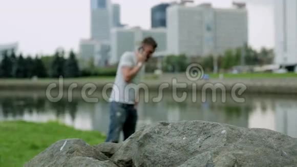 迷人的年轻人站在一块大石头附近用手机说话视频的预览图