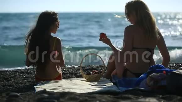 妈妈和女儿穿着泳衣留着长发在海浪背景下的海边吃水果和浆果视频的预览图
