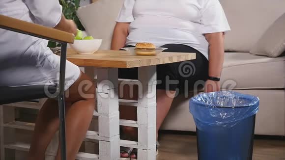一个胖女人把一个汉堡扔进垃圾桶慢慢地选择一个苹果视频的预览图