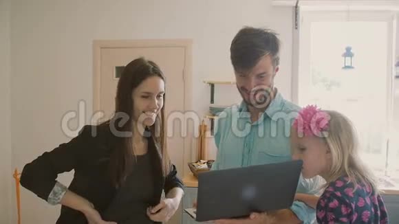 一个高大的年轻人美丽的黑发和一个可爱的金发小女孩正在看一些有趣的笔记本电脑慢节奏视频的预览图