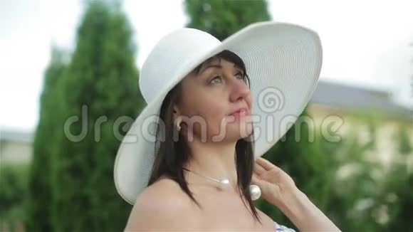 穿着连衣裙和白色太阳帽的中年妇女微笑着看着天空享受着阳光明媚的一天视频的预览图