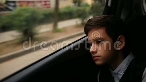 少年坐在车里看着窗外窗外闪烁着城市的树木和房屋视频的预览图