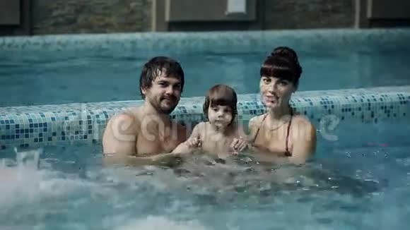 泳池里的年轻家庭父母带着儿子在游泳池里游泳和玩耍视频的预览图
