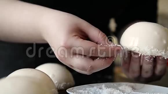 厨师用镜面釉和椰子片装饰白色摩丝蛋糕在手的框架里视频的预览图
