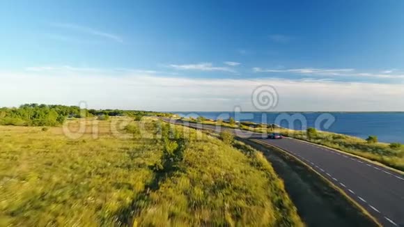 夏季日落时沿着海边的悬崖在公路上驾驶黑色汽车的鸟瞰图视频的预览图
