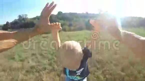 在阳光明媚的日子父亲在草地上抱起他的小儿子爸爸在大自然里和可爱的宝宝玩耍男孩牵着父母的手视频的预览图