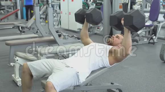 健美运动员在健身房用哑铃做长凳按压肌肉男在健身房锻炼视频的预览图