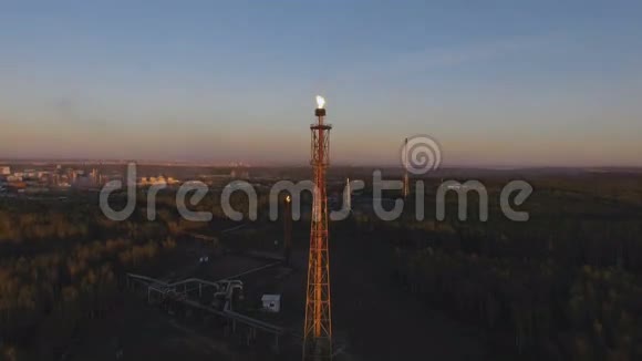 日落时分一座塔在树林间的炼油厂上挂着火炬空中景观视频的预览图
