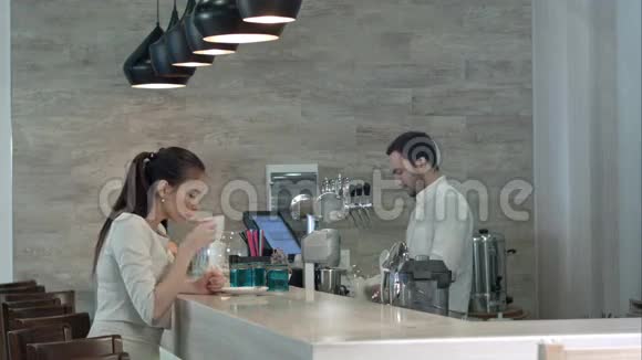 年轻女子问男咖啡师要账单坐在咖啡柜台边付款视频的预览图