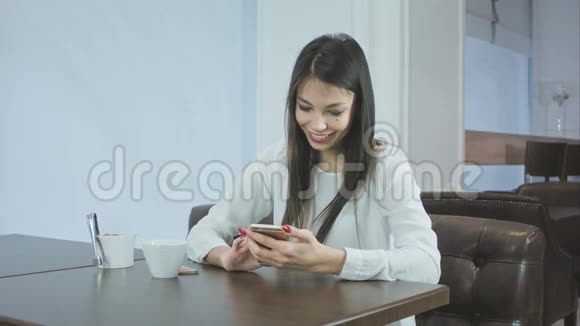 微笑的漂亮女人在咖啡馆里检查她的手机视频的预览图