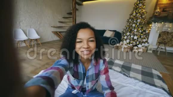年轻的非裔美国人女孩在圣诞节的时候在家里用智能手机摄像头在线聊天视频的预览图