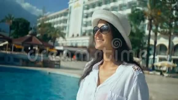 美丽的年轻女子长发在游泳池附近散步在阳光下旅游度假视频的预览图