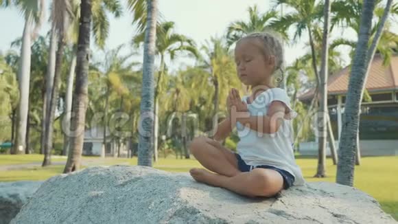 小女孩在美丽的公园里冥想背景是棕榈树视频的预览图