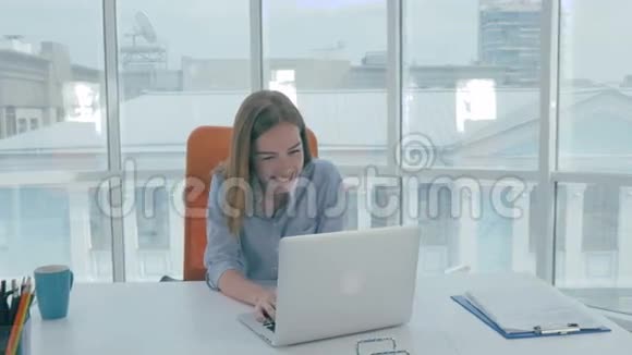 年轻漂亮的商务女性坐在现代办公室的一张桌子上用笔记本电脑工作微笑视频的预览图