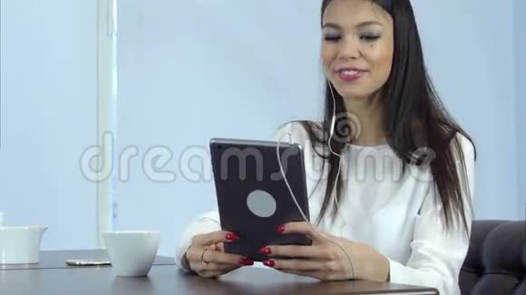 戴着耳机的微笑女人在咖啡馆里通过数码平板电脑进行视频通话视频的预览图