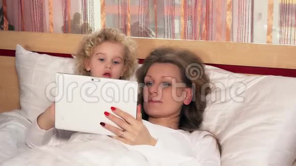 白种人小女孩和母亲床上有平板电脑视频的预览图