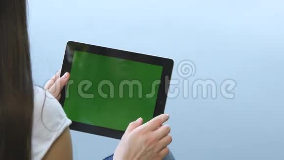 年轻女孩使用数字平板电脑和绿色屏幕坐在湖边的木制码头后景视频的预览图