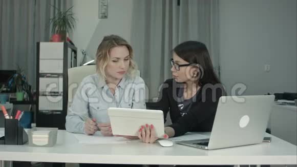 两名女性专业人员在办公桌上使用数字平板电脑视频的预览图