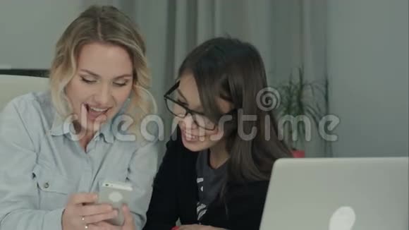 两个办公室的女孩笑着玩着看着电话视频的预览图