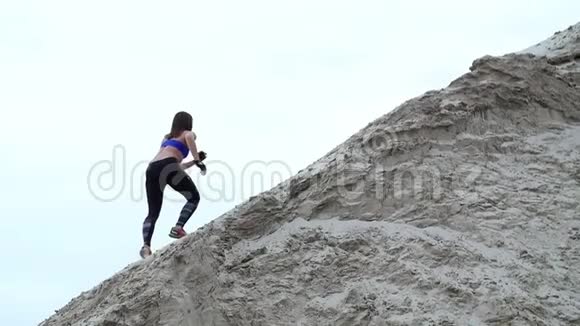 年轻女子运动员爬上一座沙山背景上可以看到货吊货港黎明视频的预览图