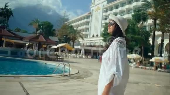 美丽的年轻女子长发在游泳池附近散步在阳光下旅游度假视频的预览图