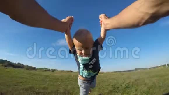 在一个阳光明媚的日子里父亲在草地上旋转他的小儿子爸爸在大自然中旋转可爱的婴儿男孩握着手视频的预览图