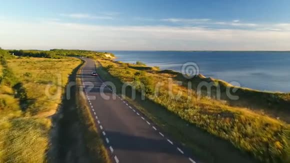 夏季日落时沿着海边的悬崖在公路上驾驶黑色汽车的鸟瞰图视频的预览图