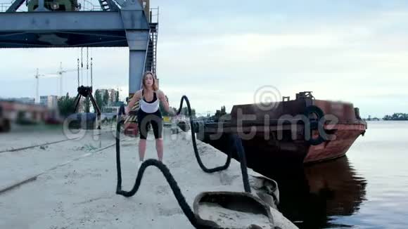 年轻的运动的女人的在一运动的绳子的帮助下进行力量练习黎明时分沿着沙滩码头视频的预览图