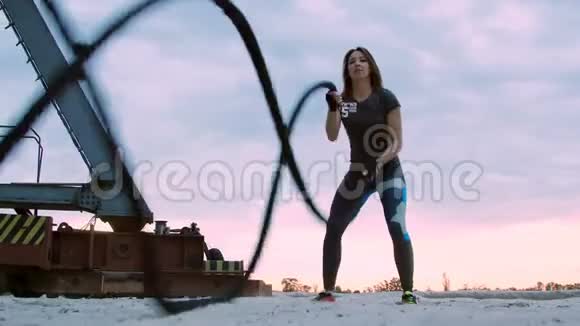 年轻的运动的女人的在一运动的绳子的帮助下进行力量练习黎明时分沿着沙滩码头视频的预览图