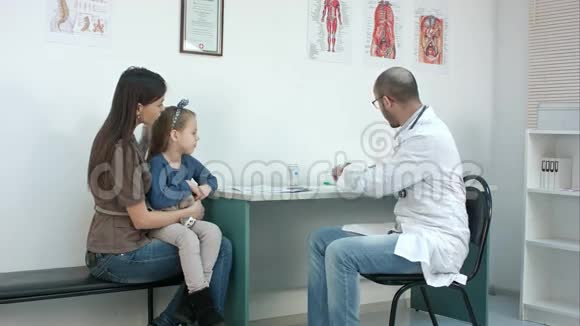 男儿科医生检查小女孩与母亲坐在一起的喉咙视频的预览图