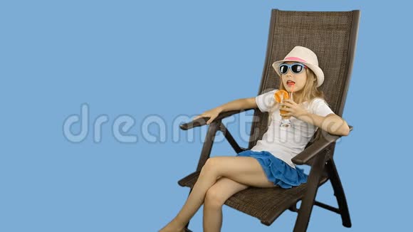 年轻的白种人女孩坐在椅子上通过吸管喝橙汁鸡尾酒视频的预览图