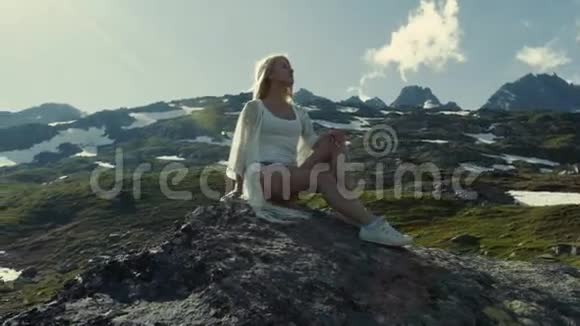 一个年轻的女孩腿漂亮坐在山顶上观察风景视频的预览图