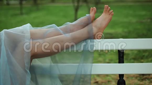 赤脚的女孩穿着蓝色裙子躺在长凳上移动脚趾在照片会议视频的预览图