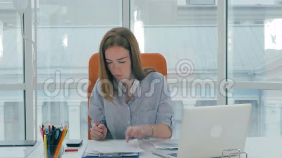 一位年轻的商务女性在现代办公室里带着电话和电脑视频的预览图