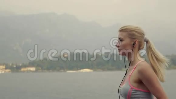 运动女孩正在湖边跑步听着耳机里的音乐动作缓慢健身风格视频的预览图