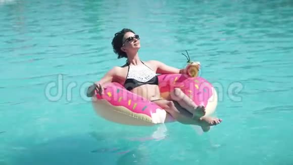 美丽的女孩戴着太阳镜日光浴躺在充气床垫甜甜圈上年轻女子喜欢放松和洗澡视频的预览图