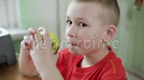 一个穿红色衬衫的男孩在厨房的桌子上吃苹果视频的预览图