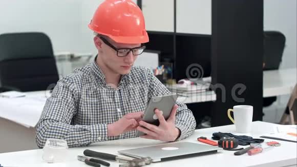办公室内使用电子平板电脑佩戴安全帽的建筑师视频的预览图
