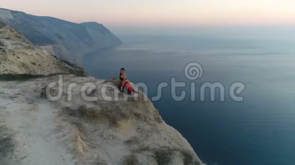 美丽的年轻女子正在山上做瑜伽担架日落时可以看到海景空中镜头视频的预览图