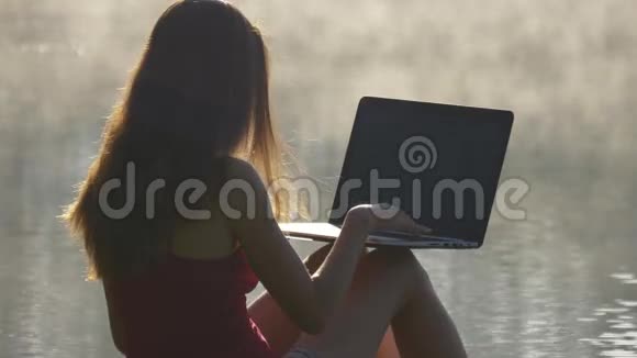 日出时女人在湖边电脑打字视频的预览图