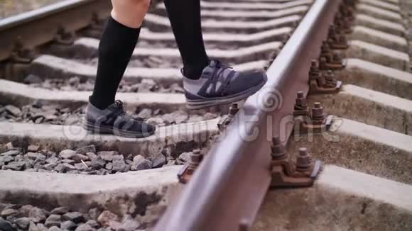 特写女性运动腿穿着黑色运动鞋和裤腿在铁轨上跳跃在铁路上在夏天女性视频的预览图