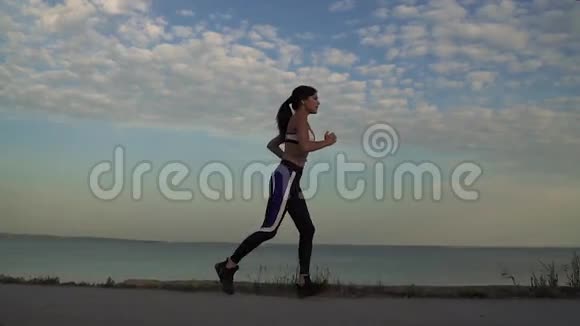 年轻女子沿着冲浪线轻轻地奔跑1女孩正在日落时慢跑视频的预览图