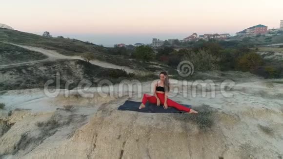 美丽的女人正在山上做瑜伽担架日落时可以看到海景空中镜头视频的预览图