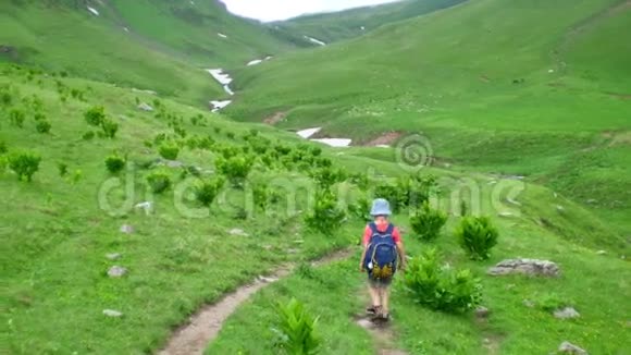 小男孩背着背包在风景秀丽的青山上徒步旅行视频的预览图
