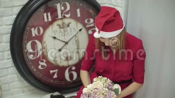 年轻的美女戴着圣诞帽手里拿着花坐在大钟附近视频的预览图