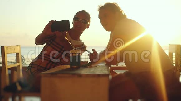 年轻漂亮的情侣在沙滩咖啡馆自拍在日落时分慢慢喝啤酒视频的预览图