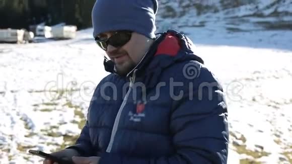 年轻有魅力的人在运动冬季服装纠正太阳镜和使用手机视频的预览图