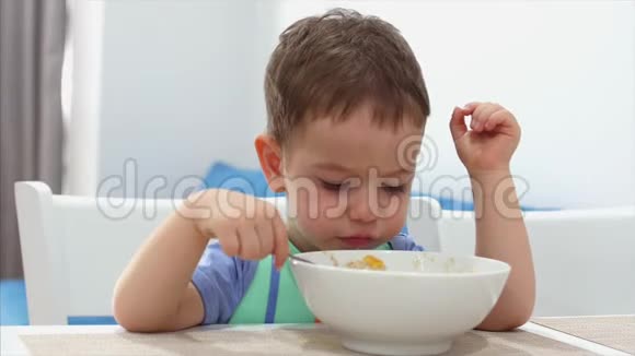 小可爱的孩子坐在一张桌子旁吃自己的燕麦片孩子吃得很自愿快乐童年的概念视频的预览图