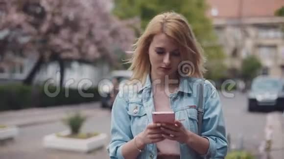 忙碌的年轻女士正在用她的手机沿街走去风的天气穿牛仔裤开车赶人和视频的预览图