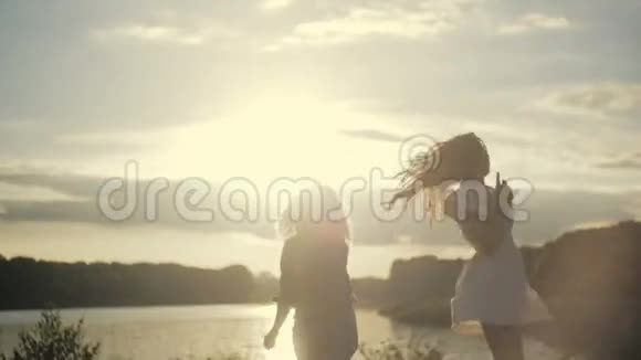 两个欧洲女孩在明亮的阳光下在湖边跳舞穿牛仔裤的卷发金发美丽的黑发视频的预览图